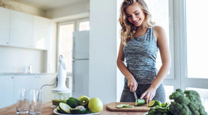 A woman cutting up some green apples on top of a table.