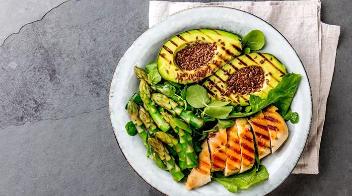 A plate of food with grilled chicken, avocado and asparagus.