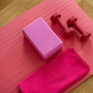A pink yoga mat with two red dumbbells and a purple block.