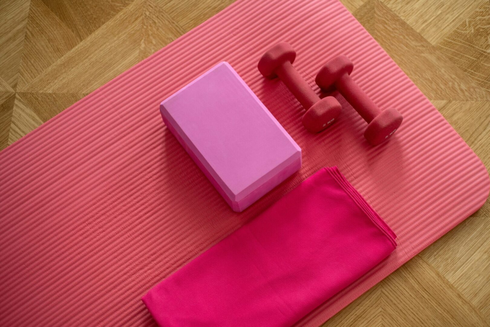 A pink yoga mat with two red dumbbells and a purple block.